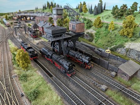 Zwei Dampfloks verschiedener Baureihen werden bekohlt, während eine weitere Lok entschlackt wird.